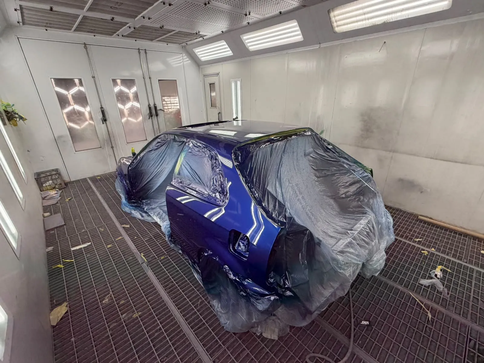 Blue classic hatchback masked up in the spray booth after a full respray