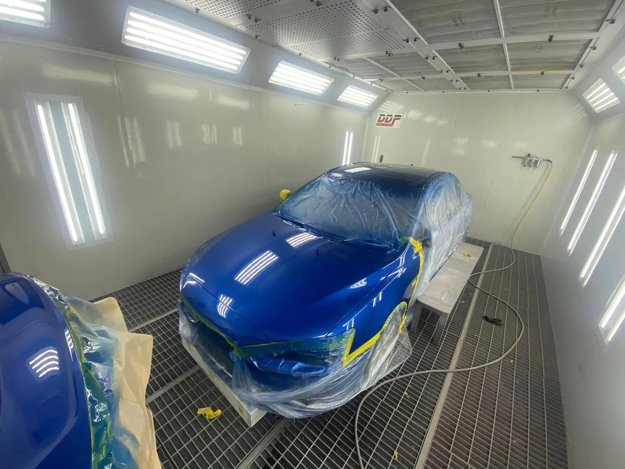 Blue sedan masked and prepped for respray in the spray booth