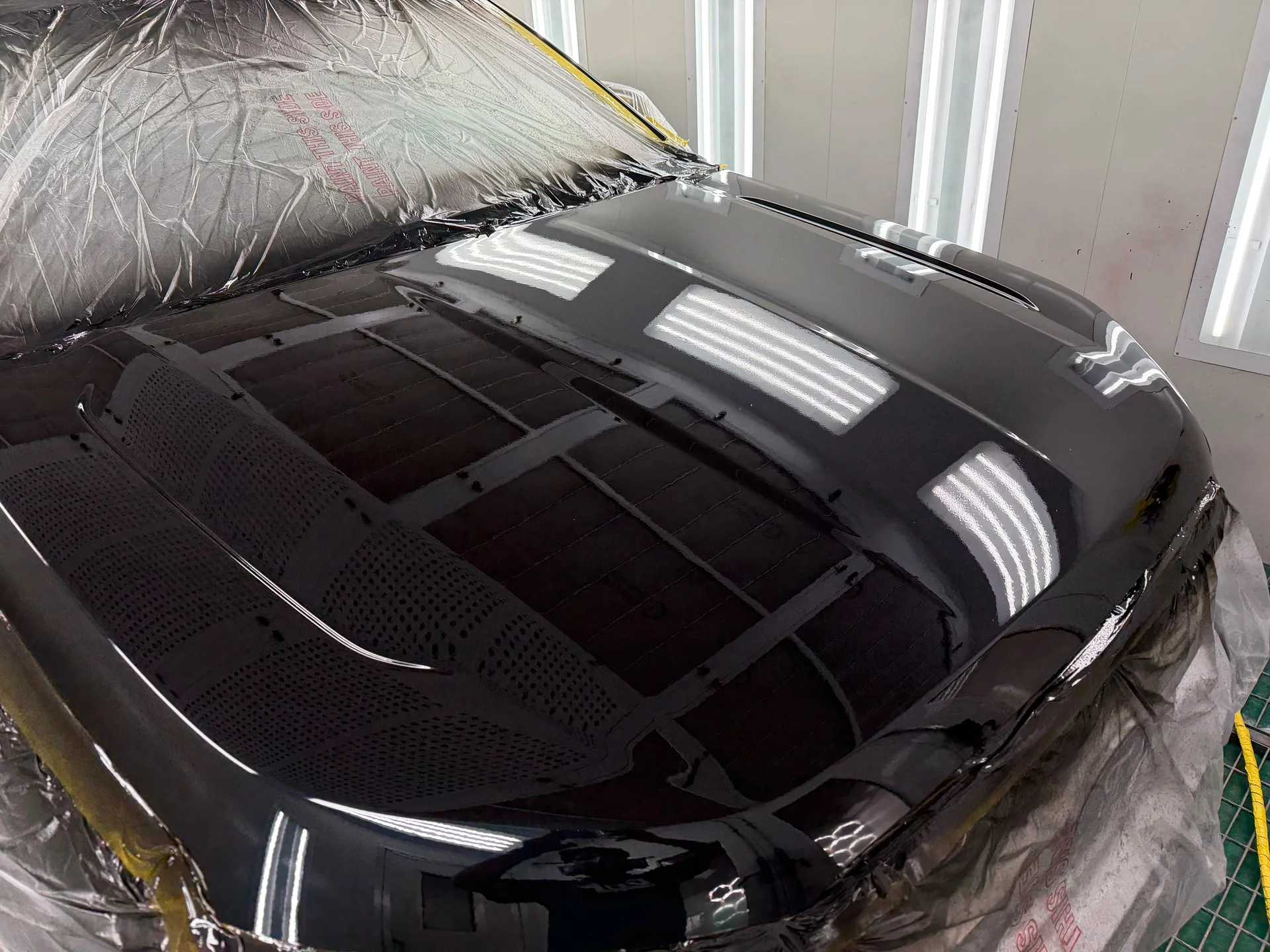 Close-up of a freshly painted dark bonnet reflecting the spray booth lights