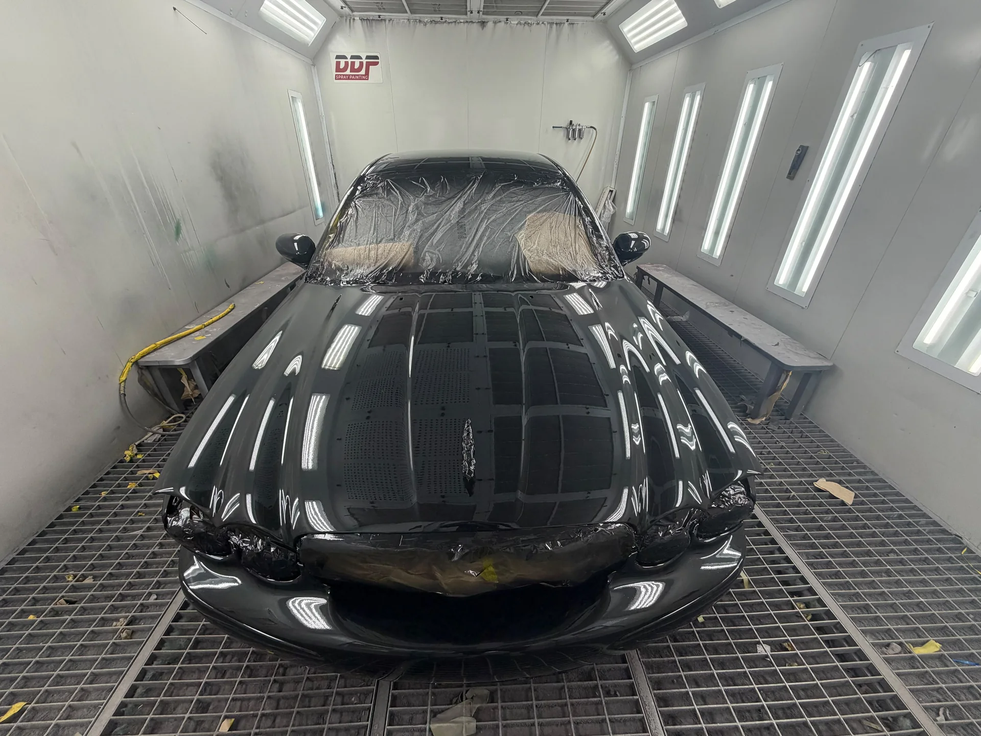 Front view of a dark Jaguar with a glossy bonnet and masked windscreen in the DDP spray booth