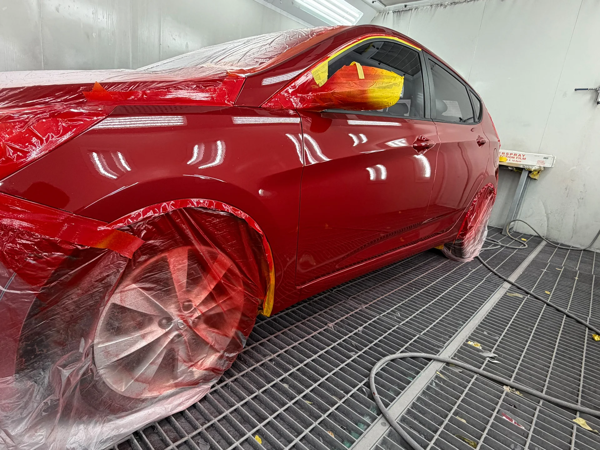 Red hatchback with freshly resprayed side panels and masked wheels in the spray booth