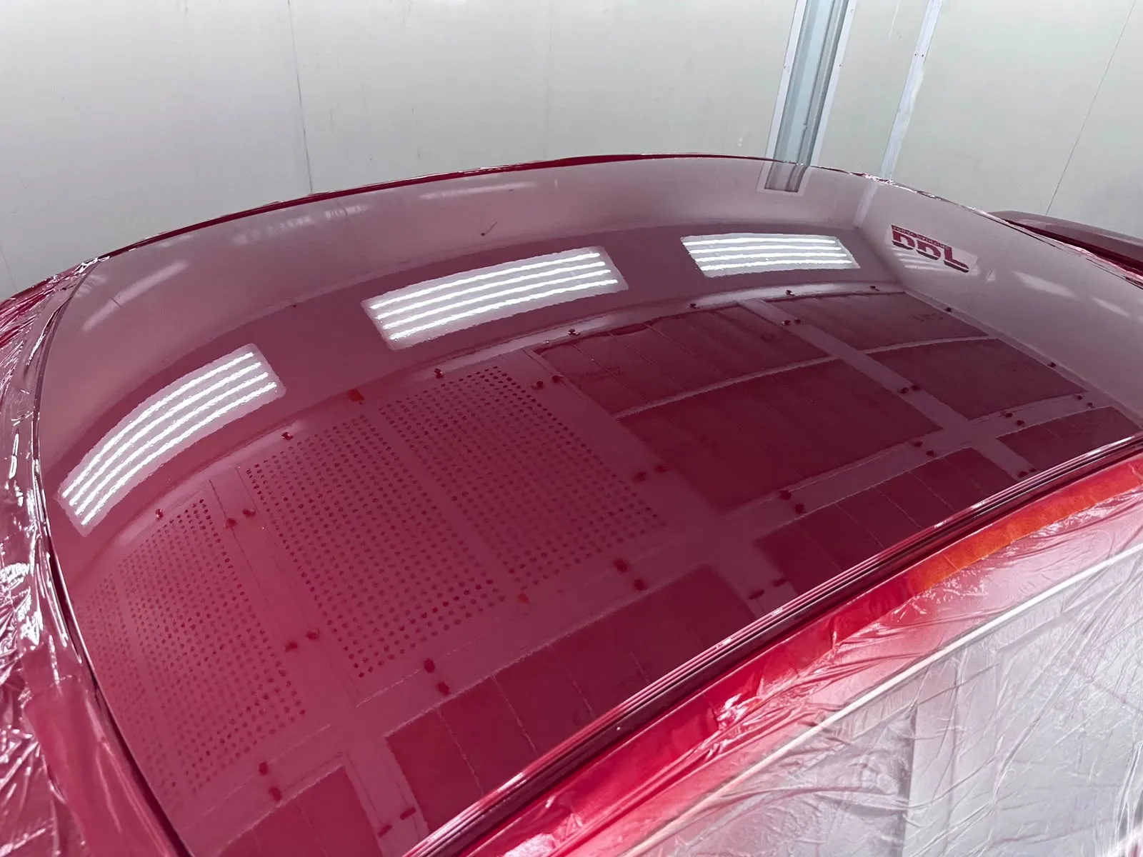 Car roof resprayed deep metallic red under the spray booth lights